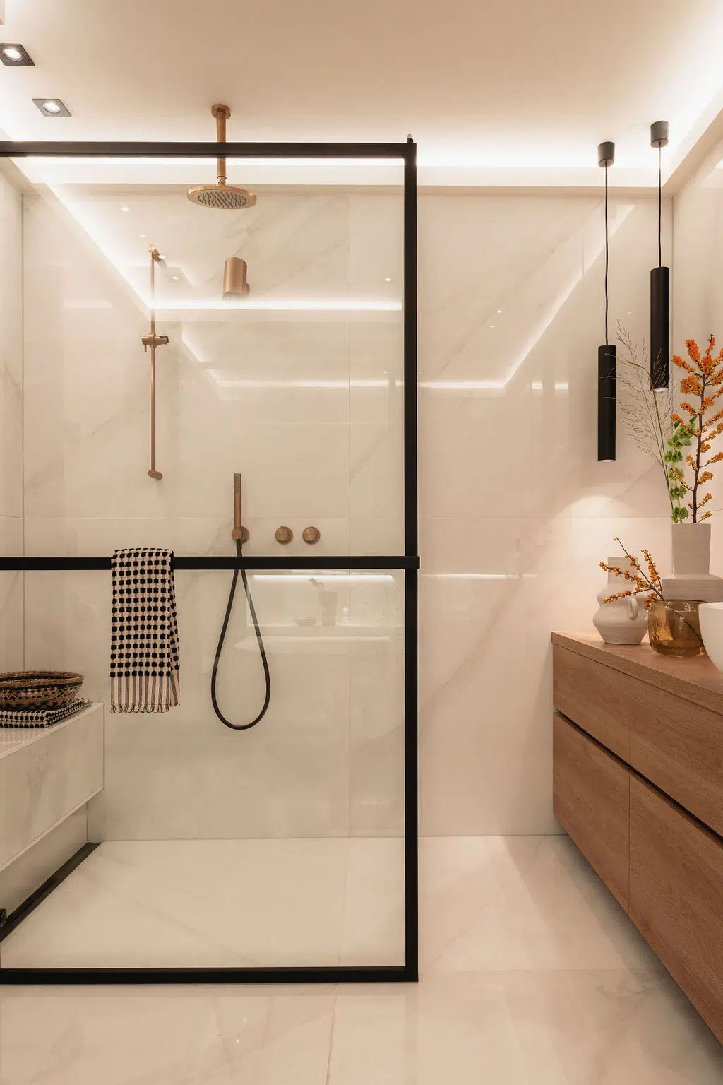 Impressie van een moderne badkamer, voorzien van inloopdouche met marmeren platen en Gessi kranen. De glazen douchewand heeft zwart metalen lijsten.