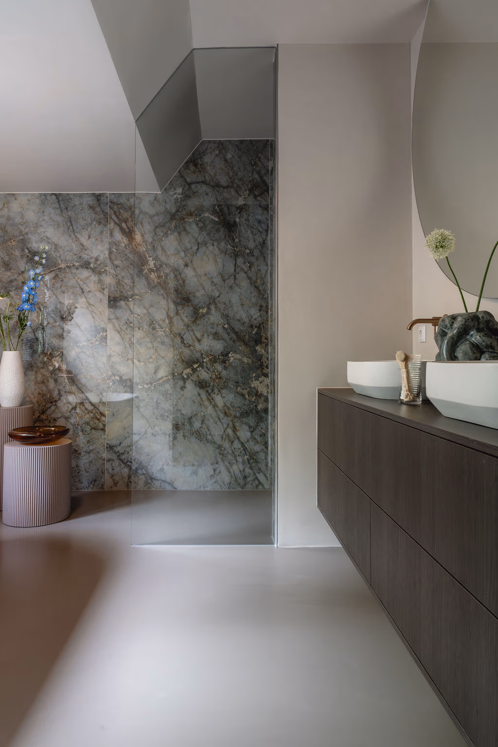 Impressie van een badkamer met donker houten badkamermeubel, Gessi kranen, een rookglas douchewand en marmerlook wandtegels in warm groen.