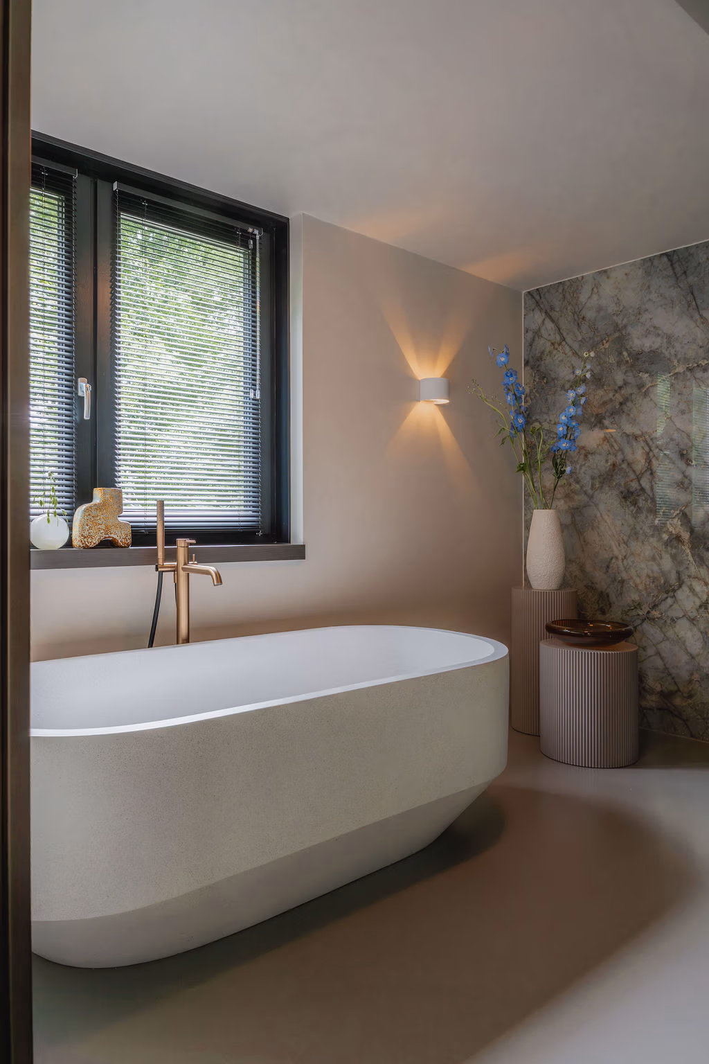 Impressie van een badkamer met handgemaakt bad, vrijstaande Gessi badkraan en marmerlook wandtegels in warm groen.